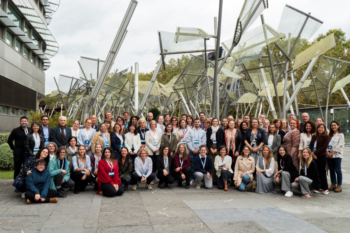The JA PRISM group is gathered in a portraite. In the background is an outdoor artwork of the Guggenheim Museum in Bilbao